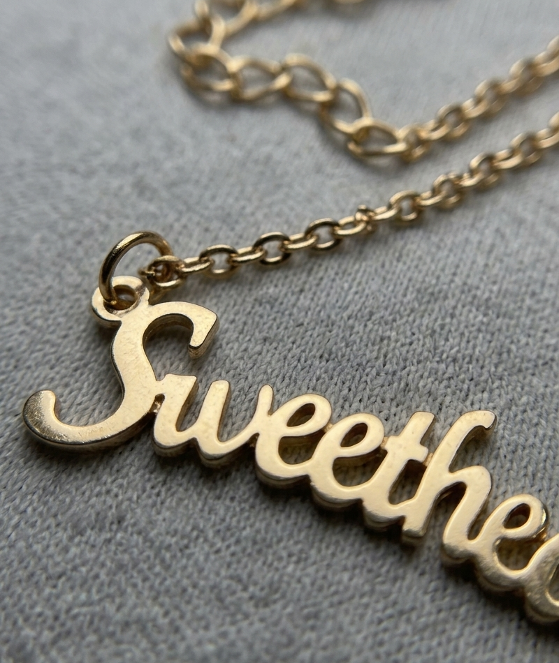 Gold necklace with 'Sweethearts' pendant on a gray background