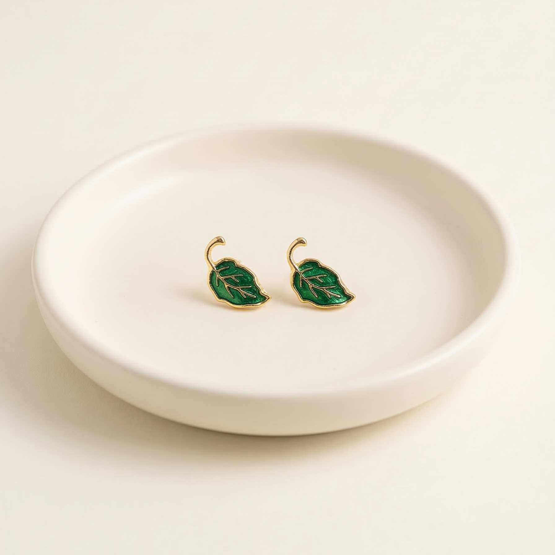 Green leaf-shaped earrings on a white ceramic dish