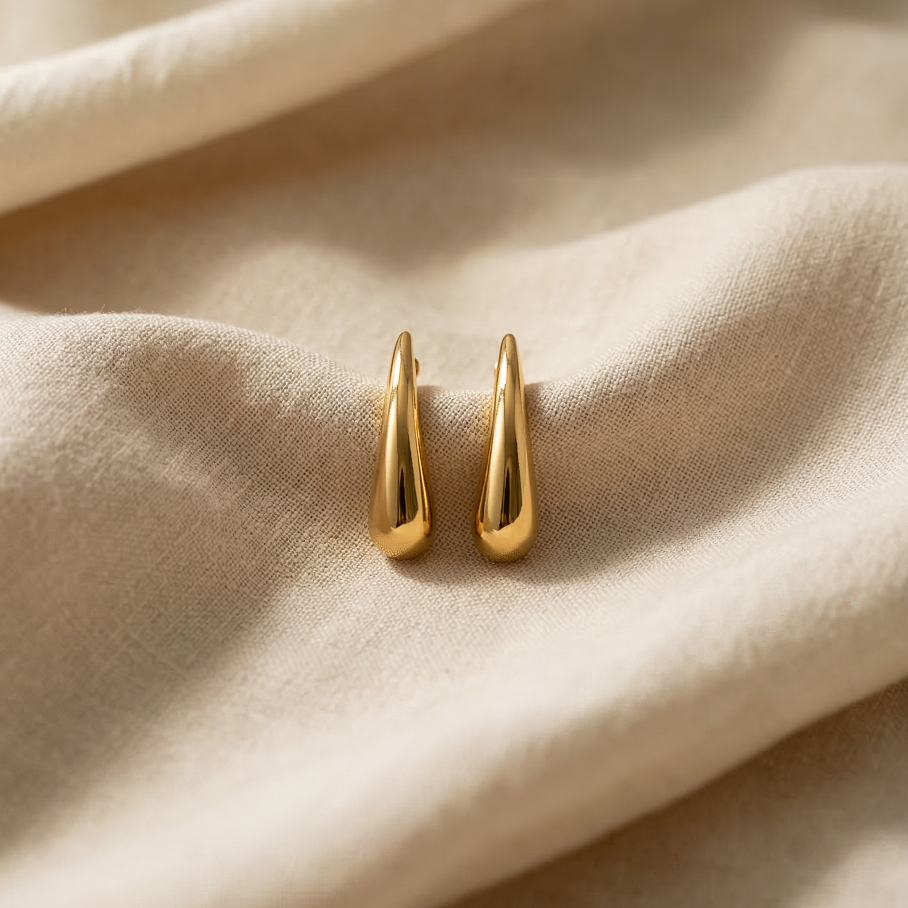 Gold earrings on a beige fabric background