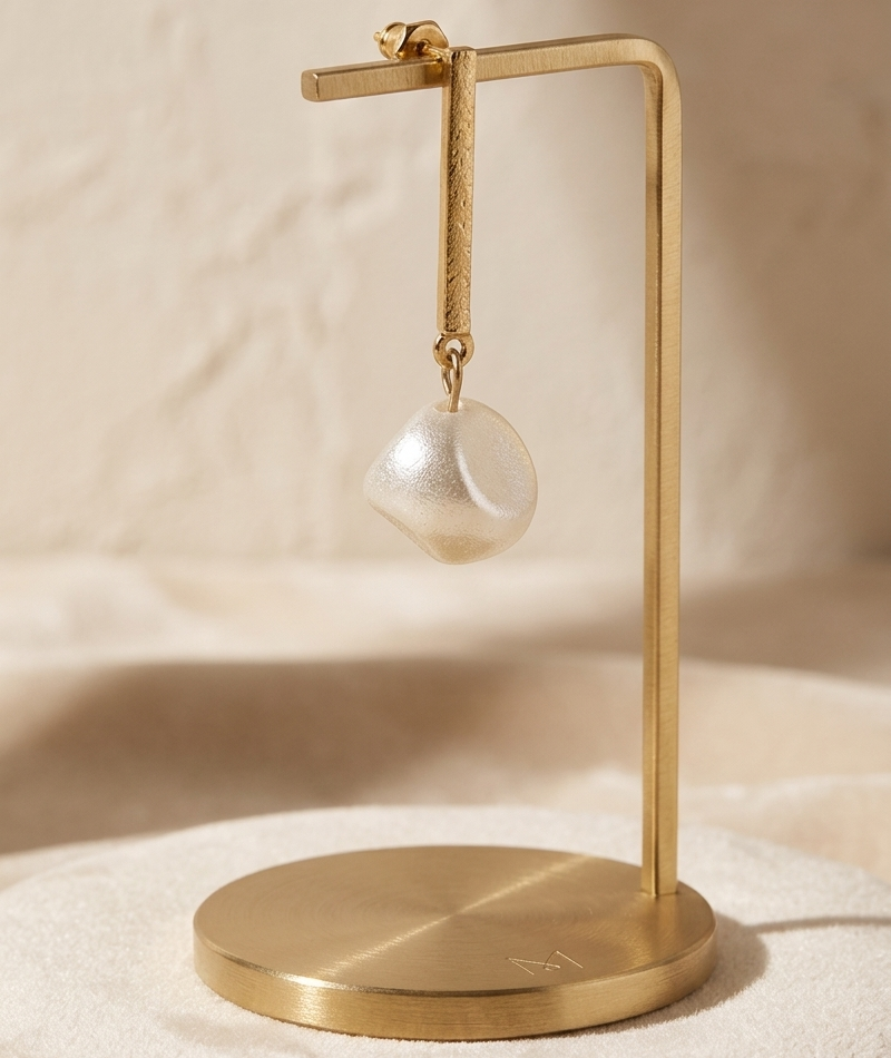 Gold jewelry stand with a single earring on a beige background