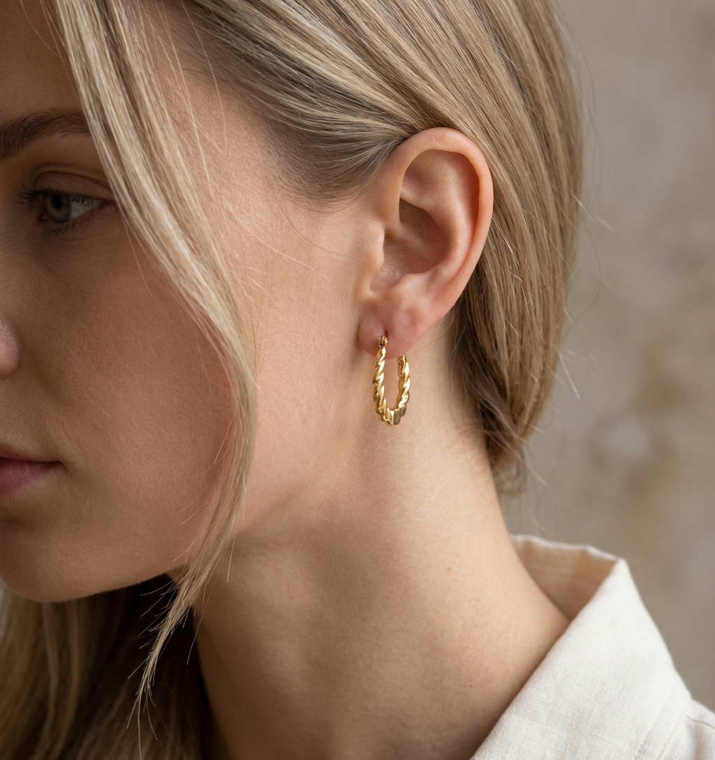 Close-up of a person wearing a gold hoop earring with a neutral background