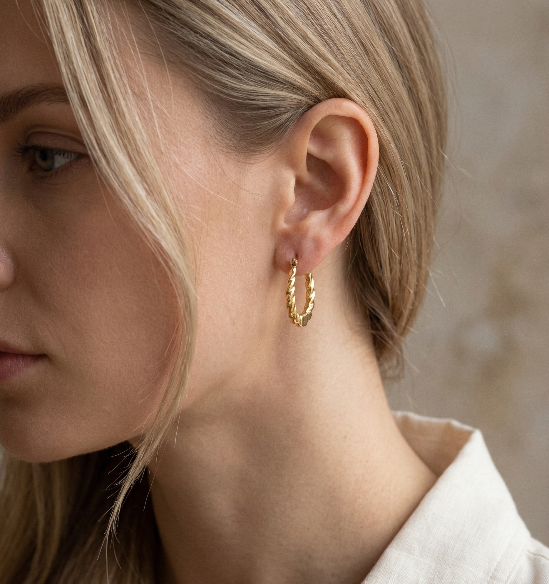 Close-up of a person wearing a gold hoop earring with a neutral background