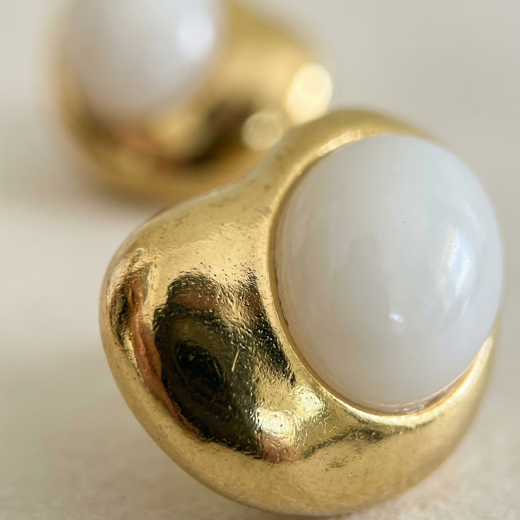 Gold earrings with white spherical stones on a light background