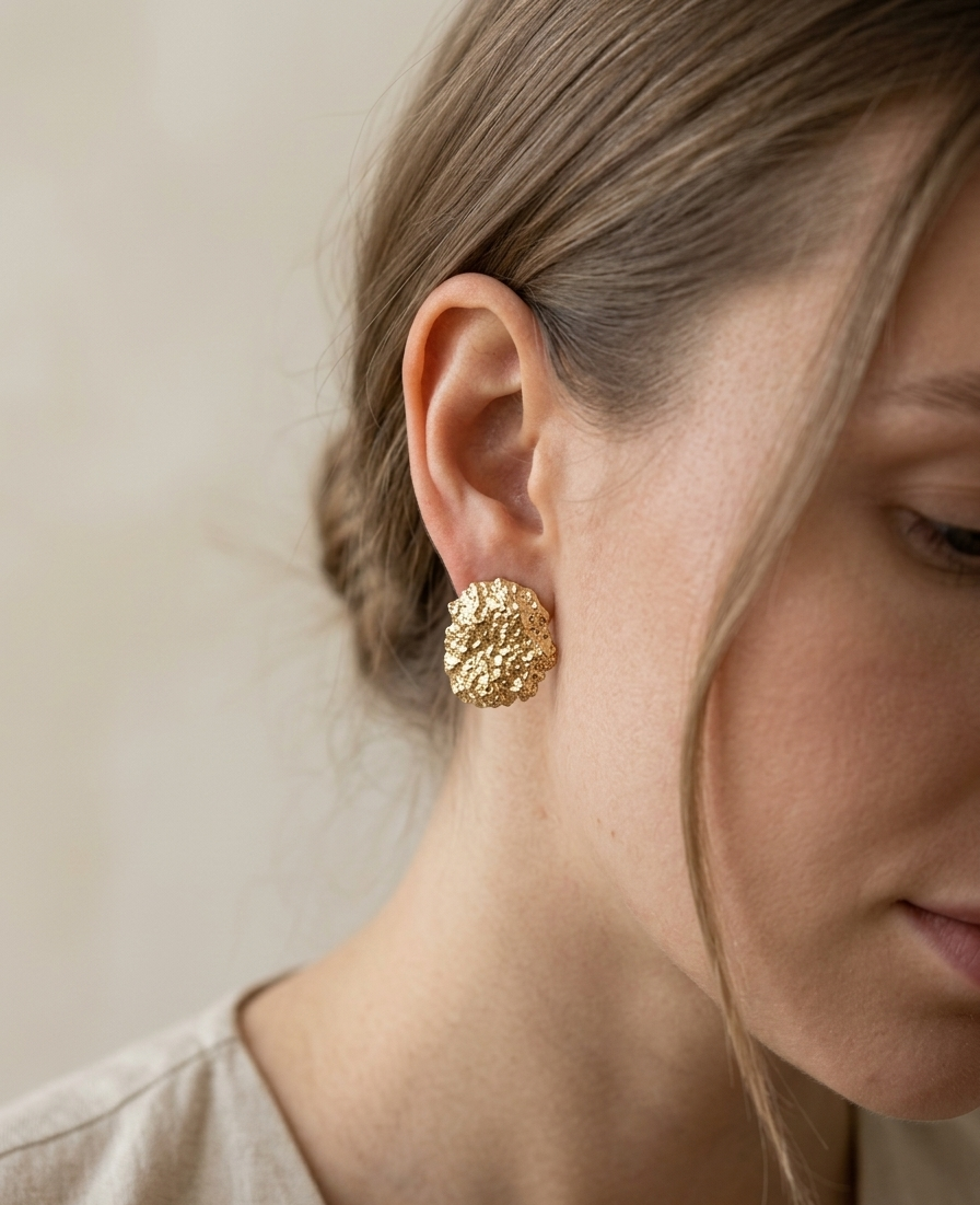Close-up of a person wearing a gold textured earring against a neutral background