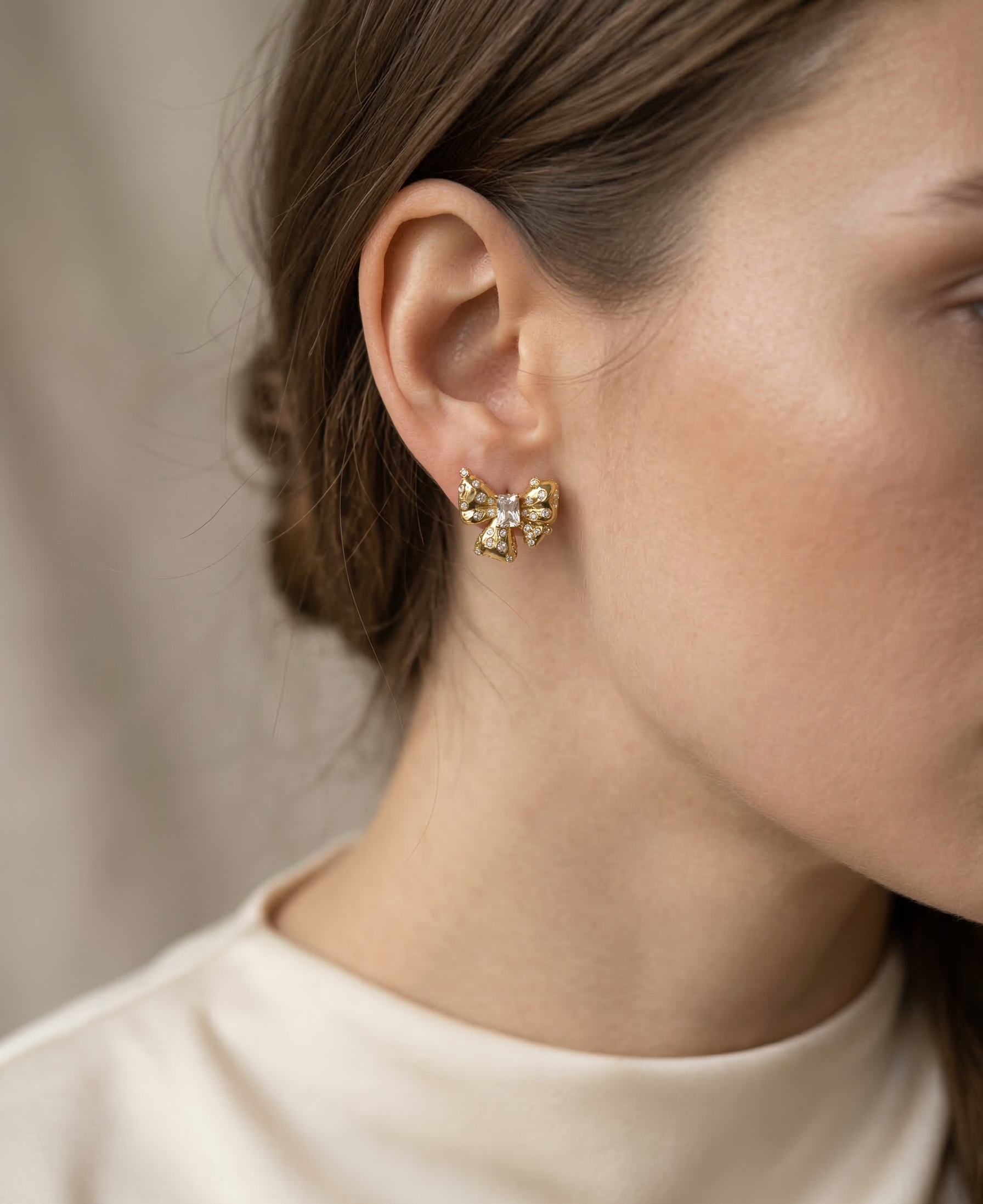 Close-up of a person wearing gold earrings with a neutral background