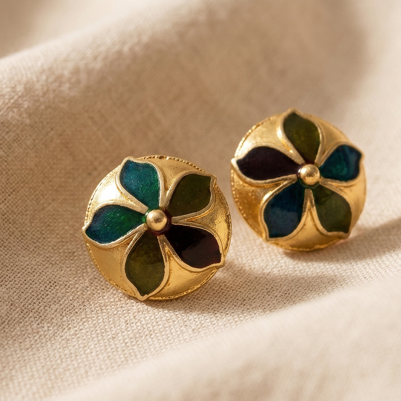 Gold earrings with green gemstones on a beige fabric background