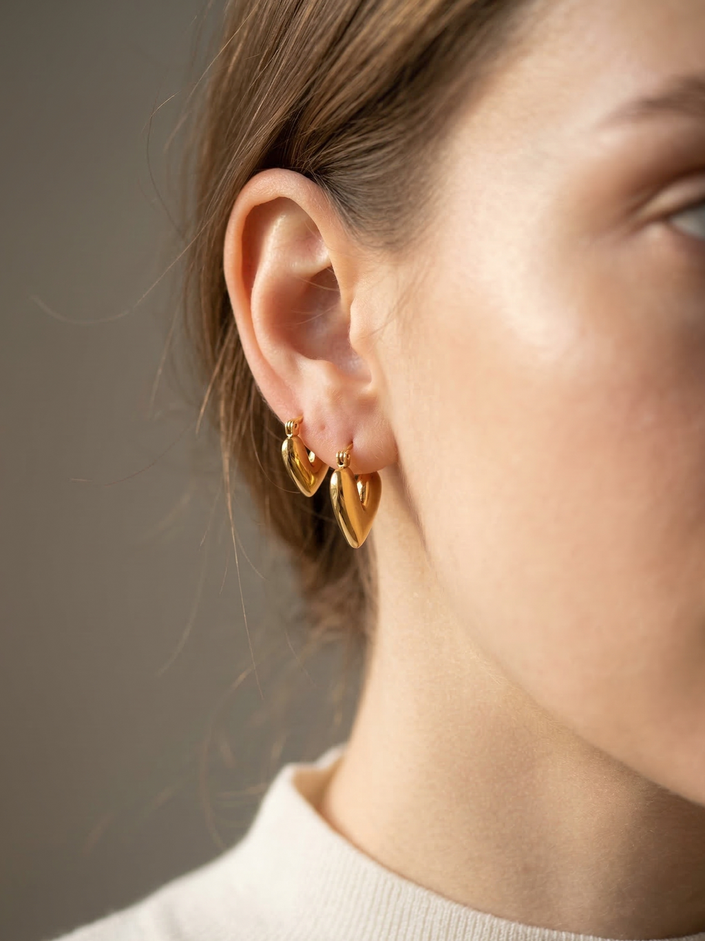 Close-up of a person wearing gold heart-shaped earrings against a neutral background