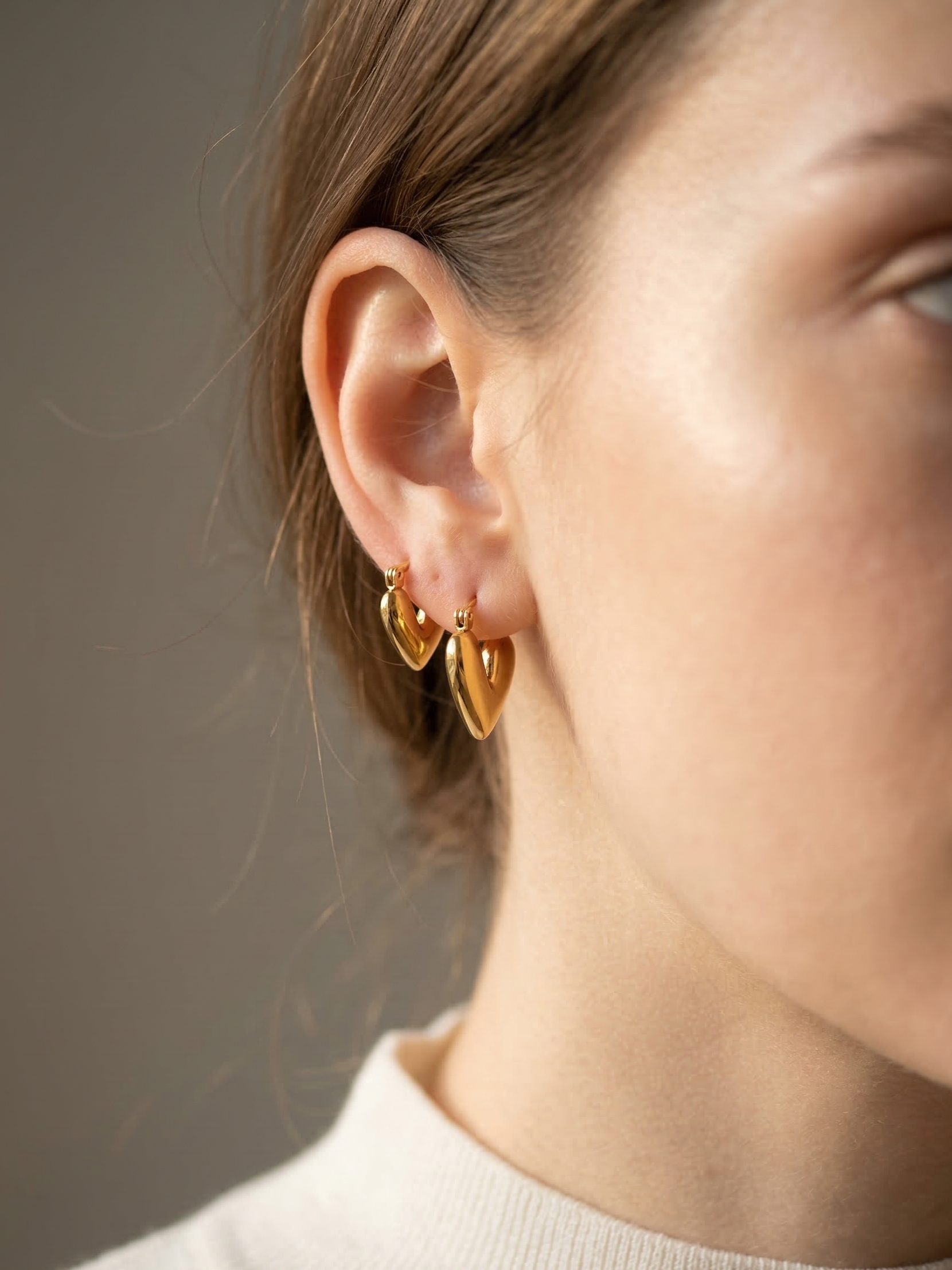 Close-up of a person wearing gold heart-shaped earrings against a neutral background
