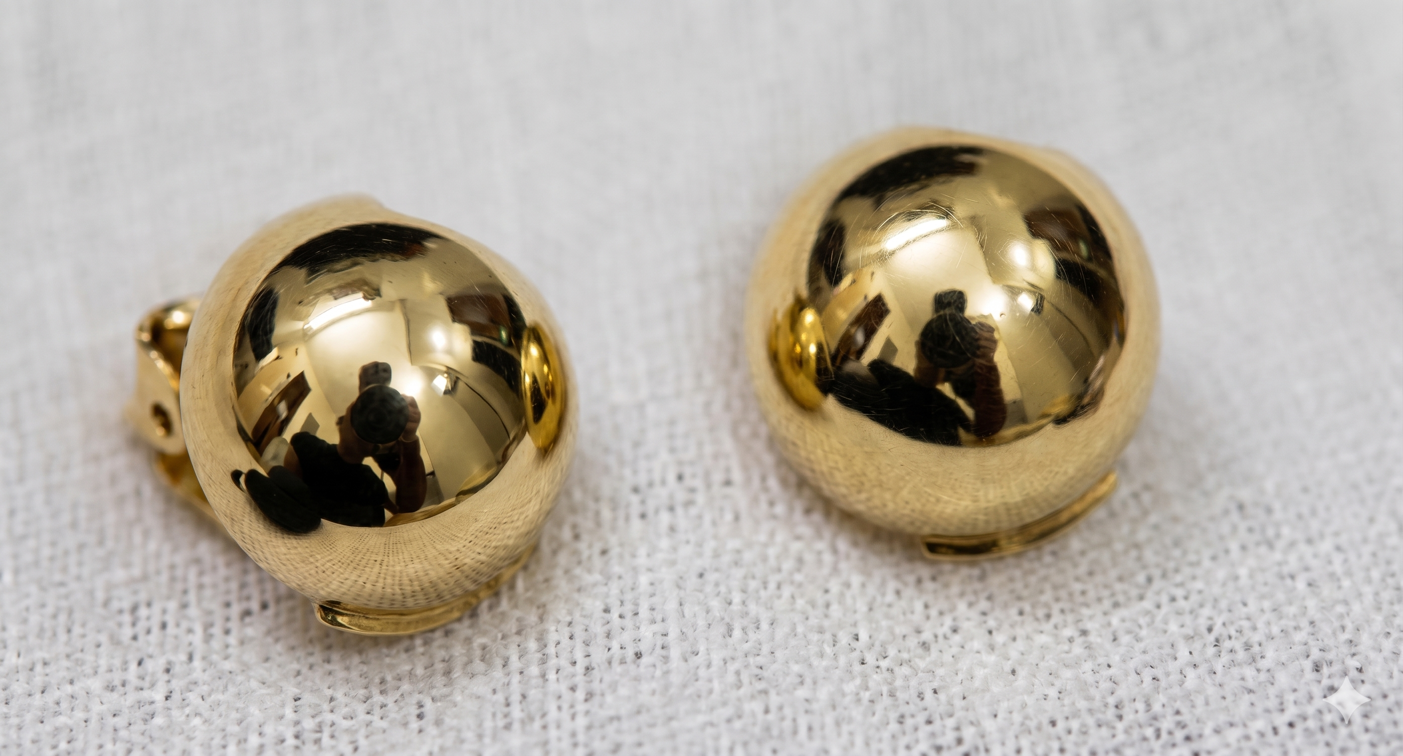 Pair of gold spherical earrings on a textured white background