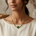Woman wearing a gold necklace with a green pendant against a neutral background