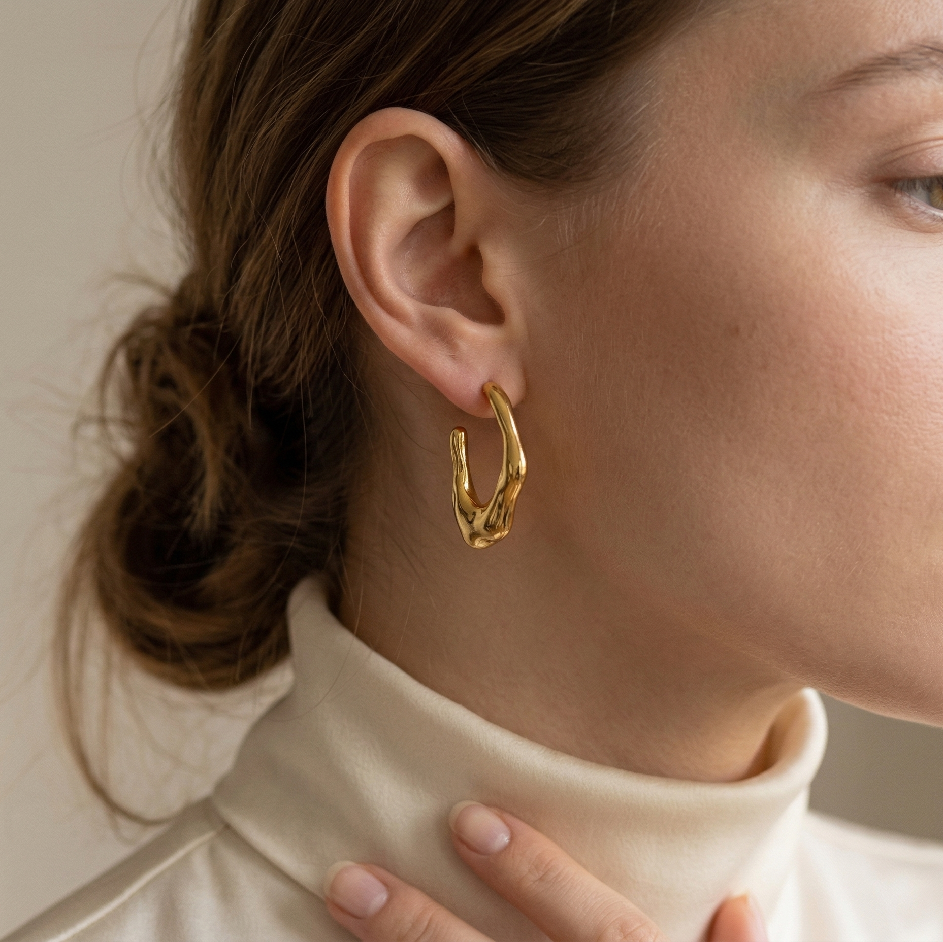 Close-up of a woman wearing gold hoop earrings with a neutral background