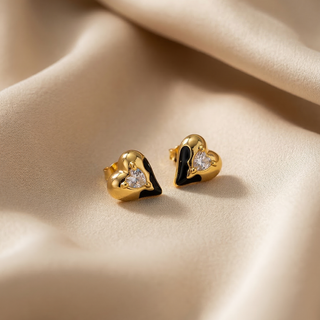 Heart-shaped gold earrings with embedded stones on a beige fabric background