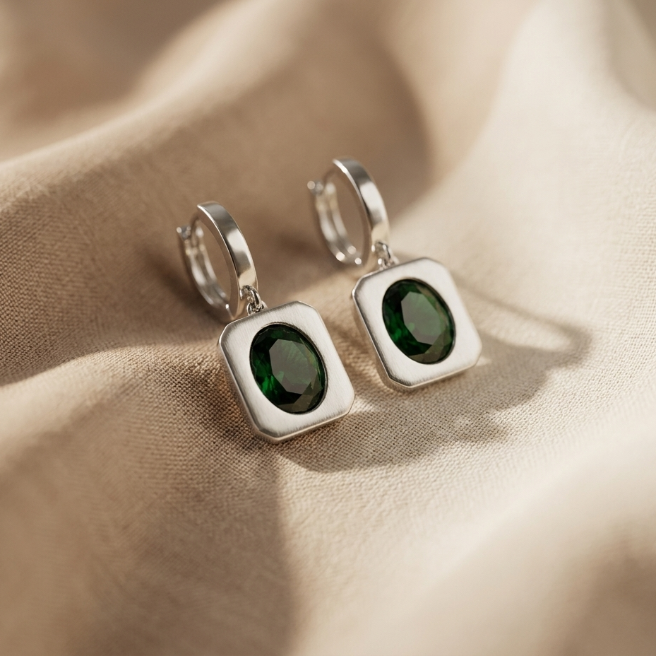Silver earrings with green gemstones on a beige fabric background