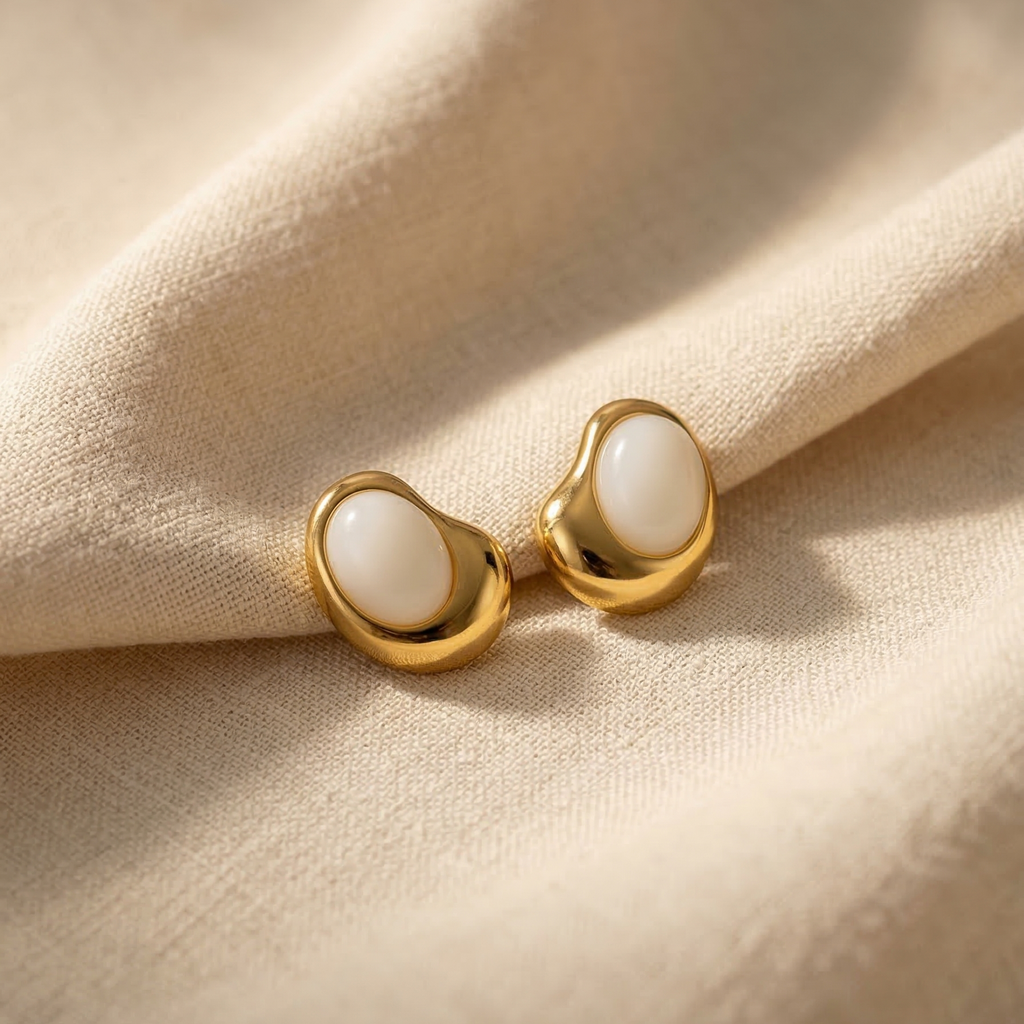 Gold earrings with white stones on a beige fabric background