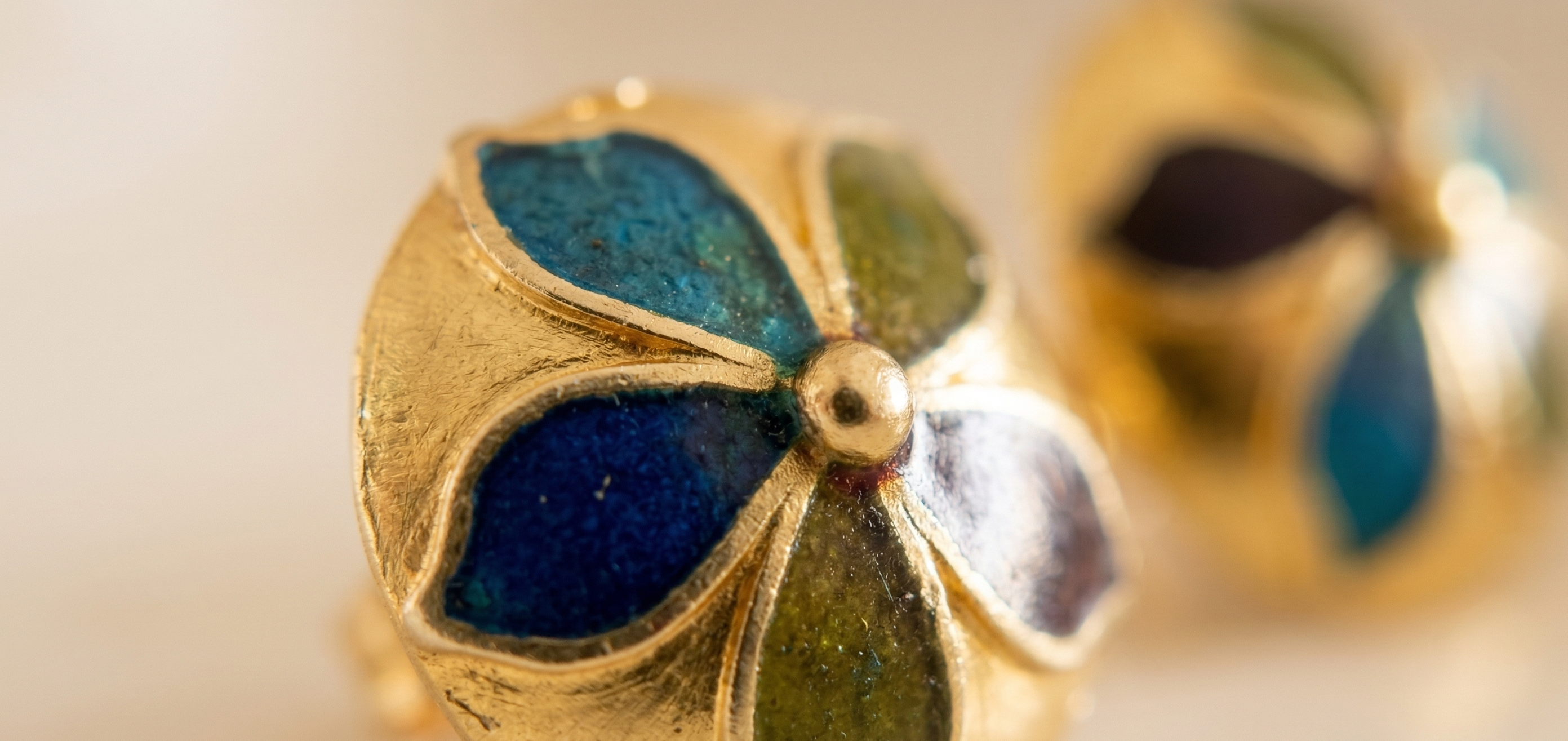 Gold earrings with blue and green enamel details on a light background