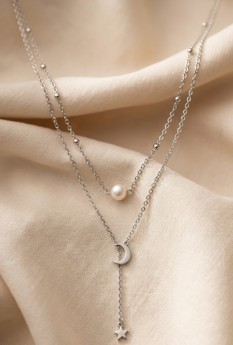 Two delicate necklaces with star and moon pendants on a beige fabric background