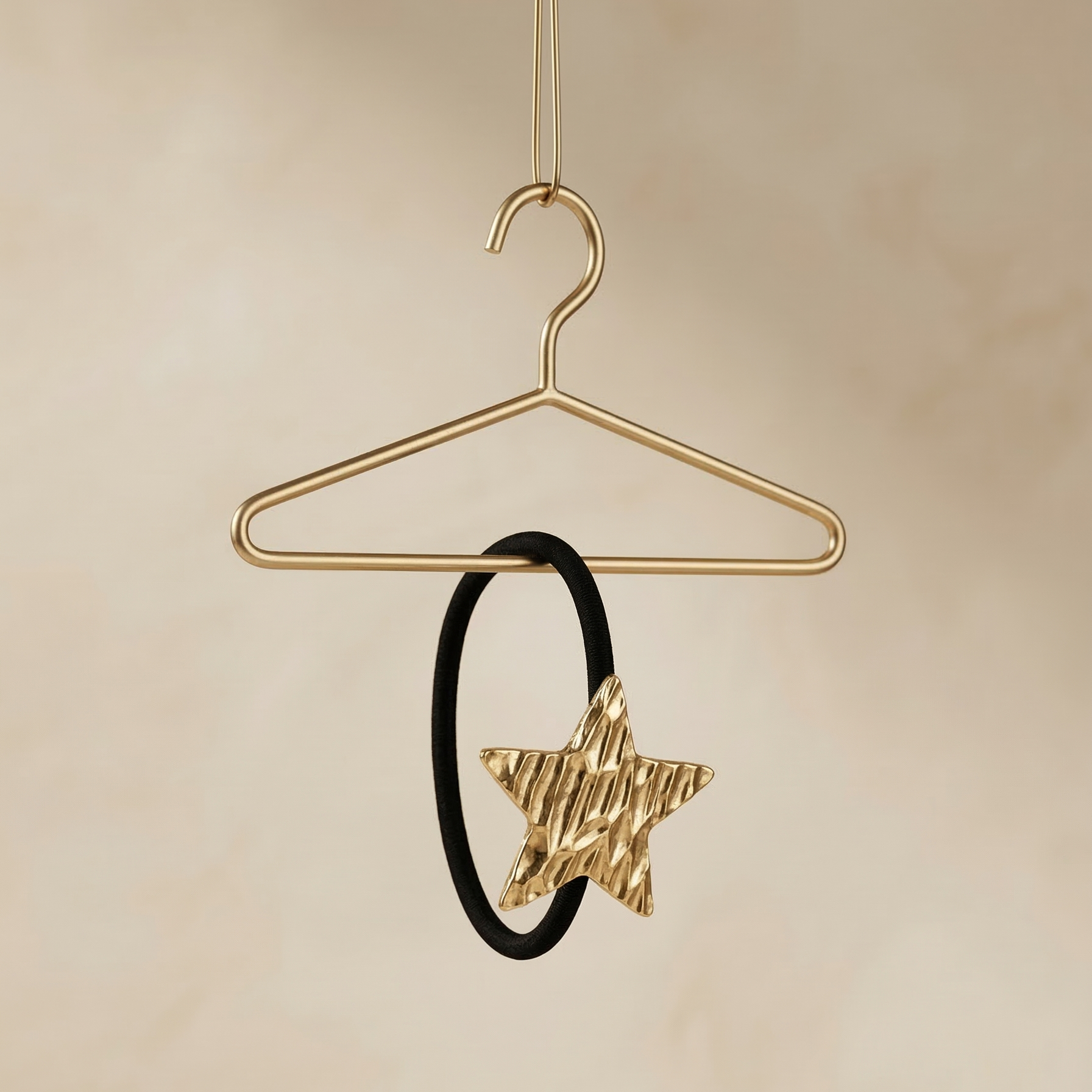 Gold star-shaped hair clip on a black hair tie hanging from a gold hanger against a beige background