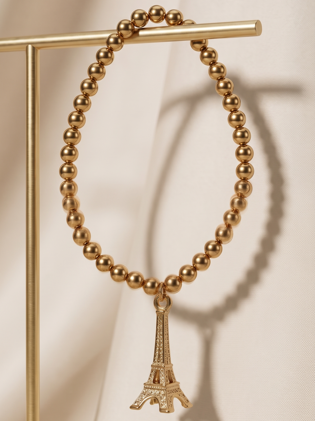 Gold beaded bracelet with Eiffel Tower charm on a beige background