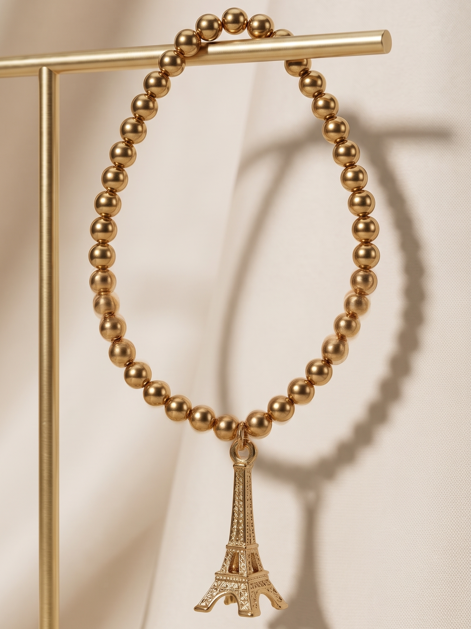 Gold beaded bracelet with Eiffel Tower charm on a beige background