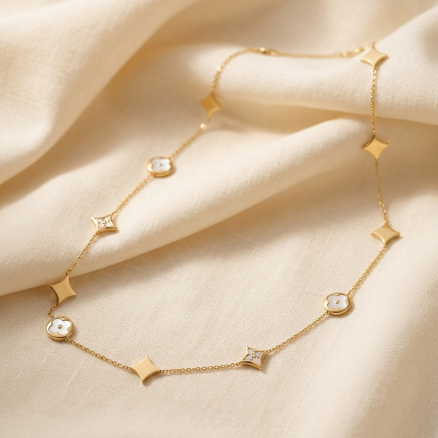 A delicate gold chain necklace draped elegantly on soft, cream-colored fabric. The necklace features alternating gold star and diamond-shaped charms, with some clear crystal accents.