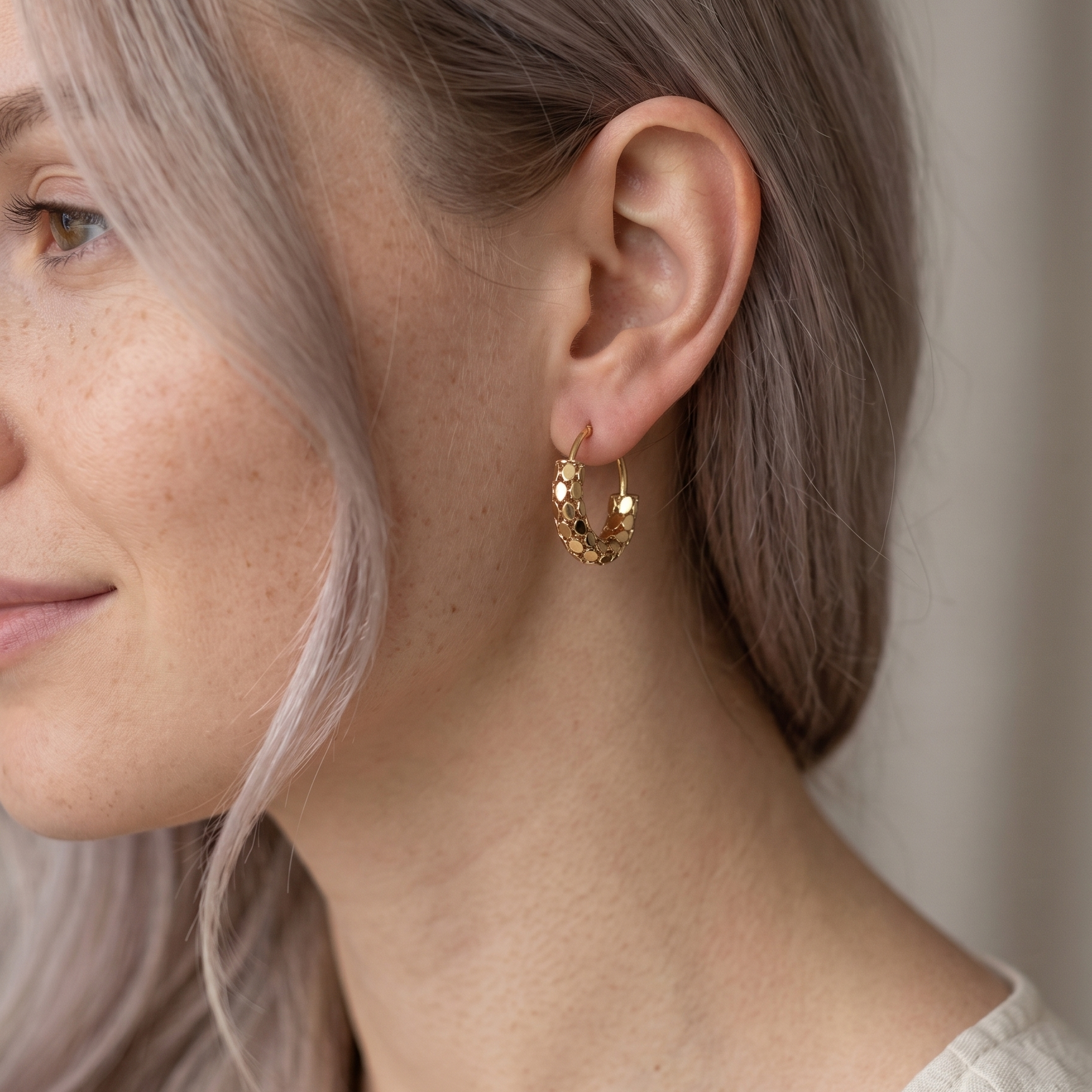 Close-up of a person wearing gold hoop earrings with a neutral background