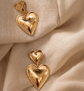 Gold heart-shaped earrings on beige fabric