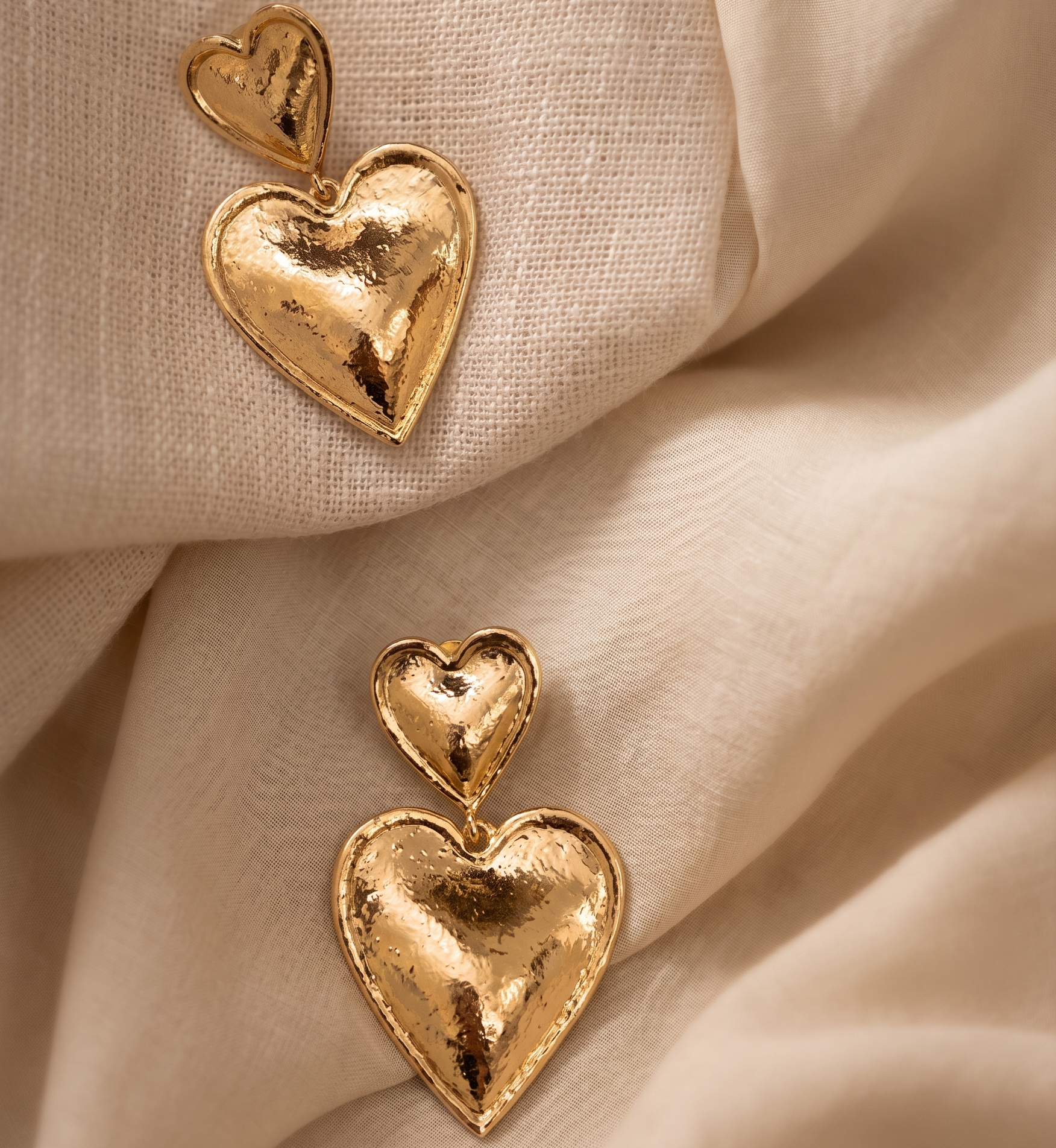 Gold heart-shaped earrings on beige fabric