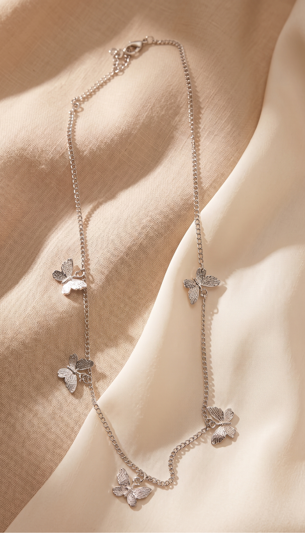 Silver butterfly necklace on a soft beige fabric background