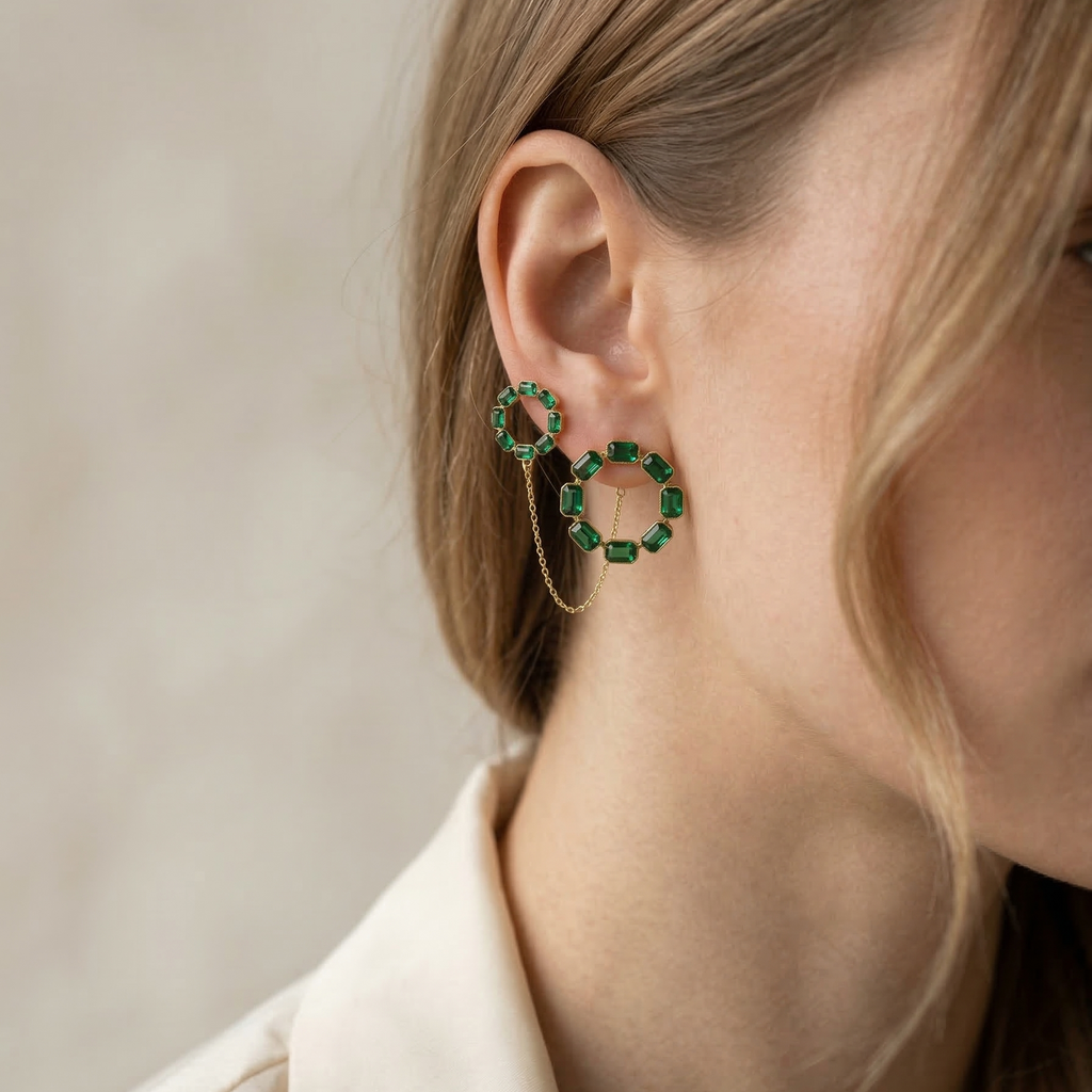 Close-up of a person wearing green hoop earrings with a neutral background