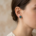 Close-up of a person wearing a blue floral earring against a neutral background