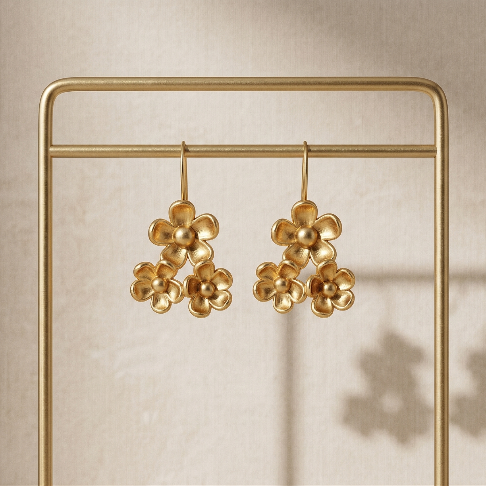 Gold floral earrings on a gold stand against a beige background