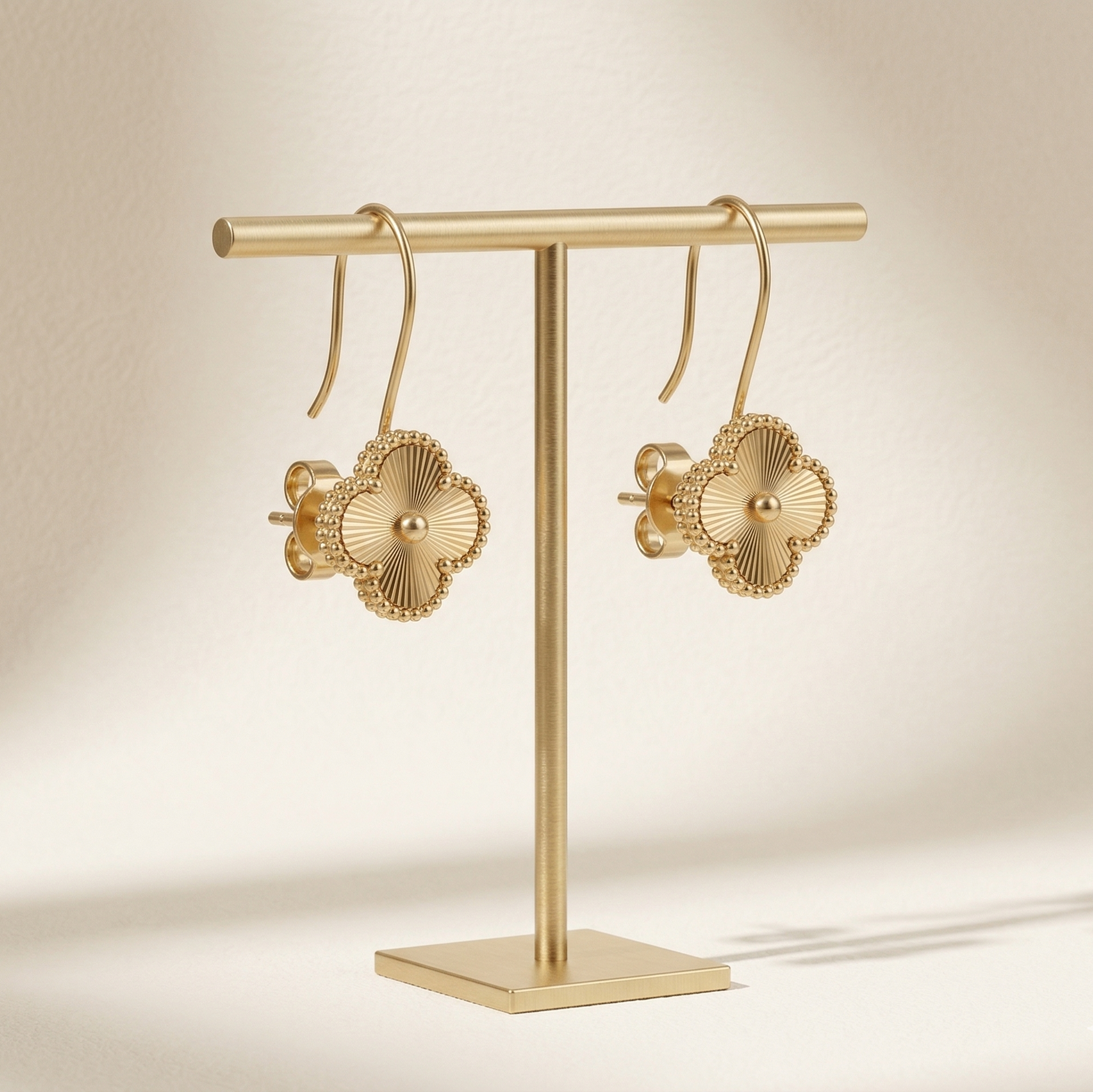 Gold earrings on a matching gold stand against a beige background