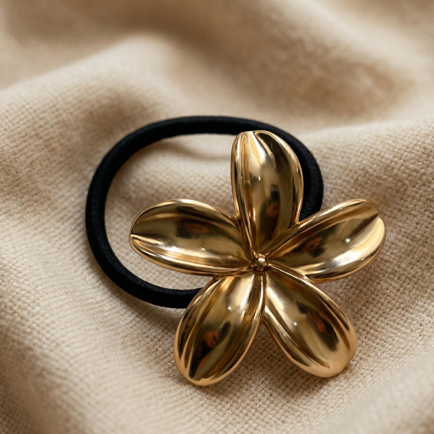 Gold flower-shaped hair tie on a beige fabric background