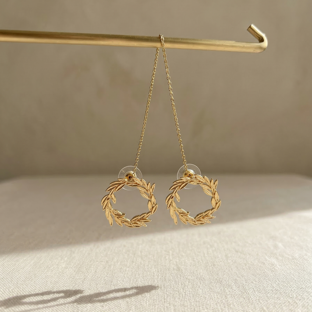 Gold wreath earrings hanging on a hook with a neutral background