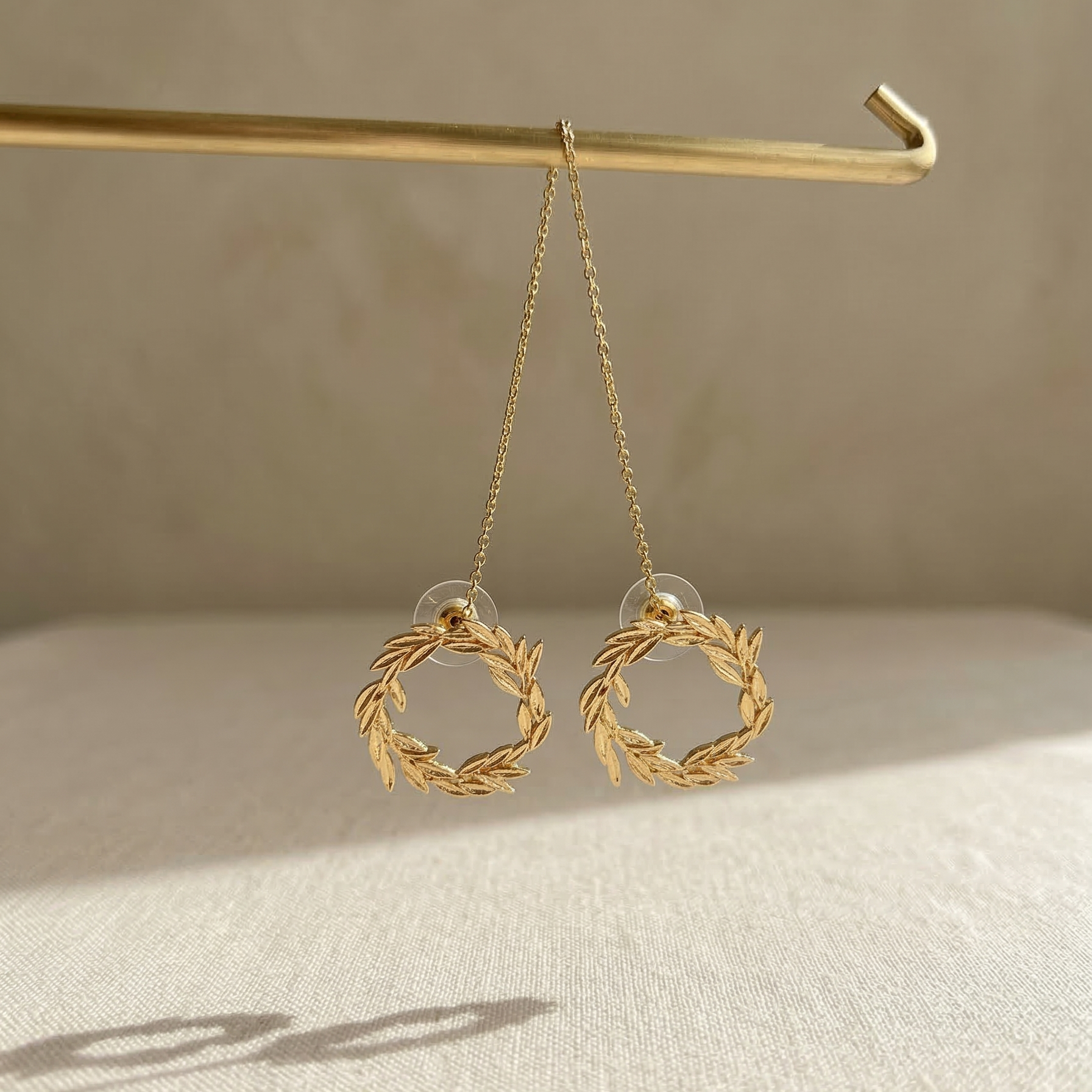 Gold wreath earrings hanging on a hook with a neutral background