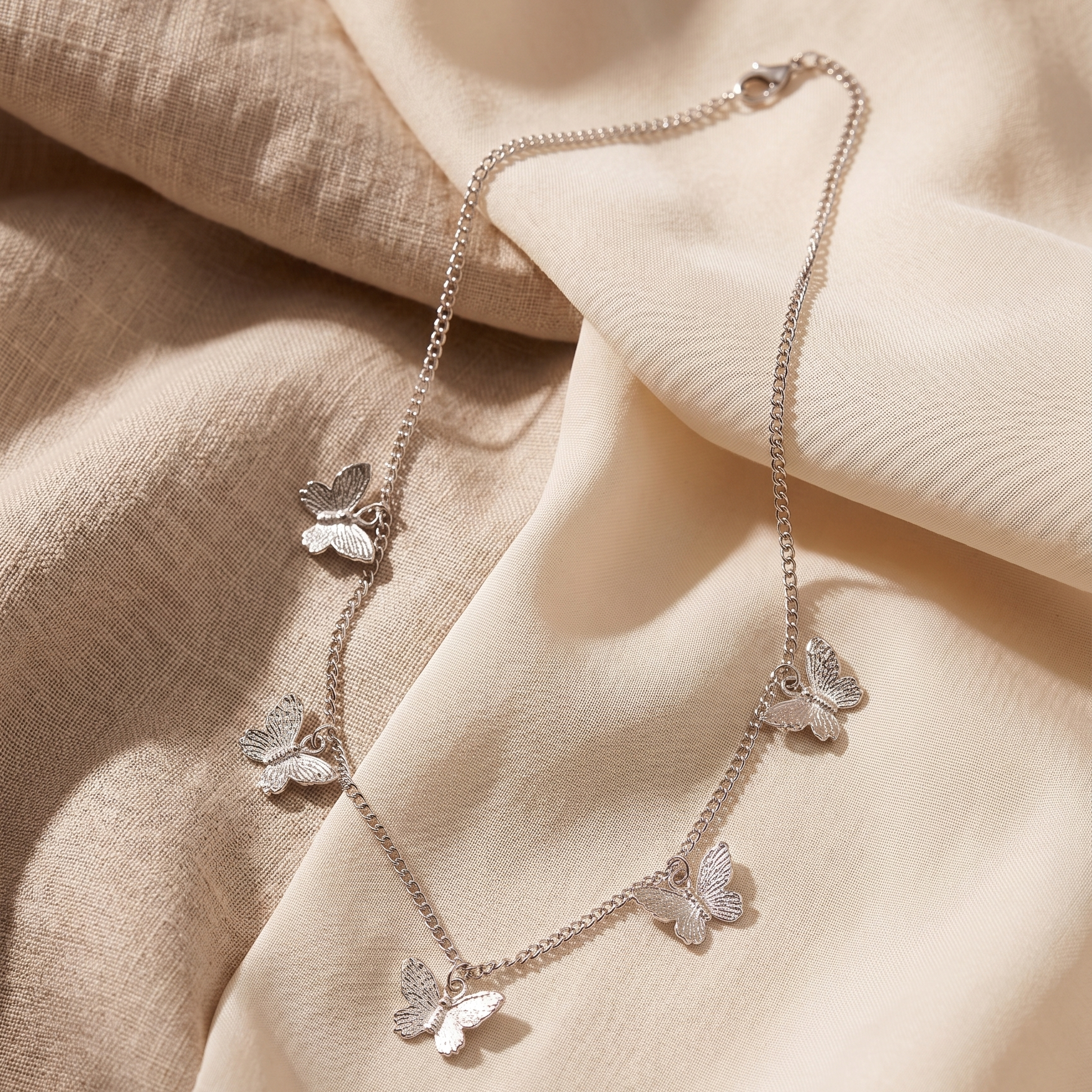Butterfly-themed necklace on a soft beige fabric background