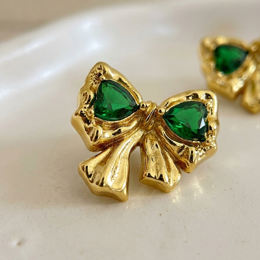 Gold bow-shaped earrings with green gemstones on a white surface