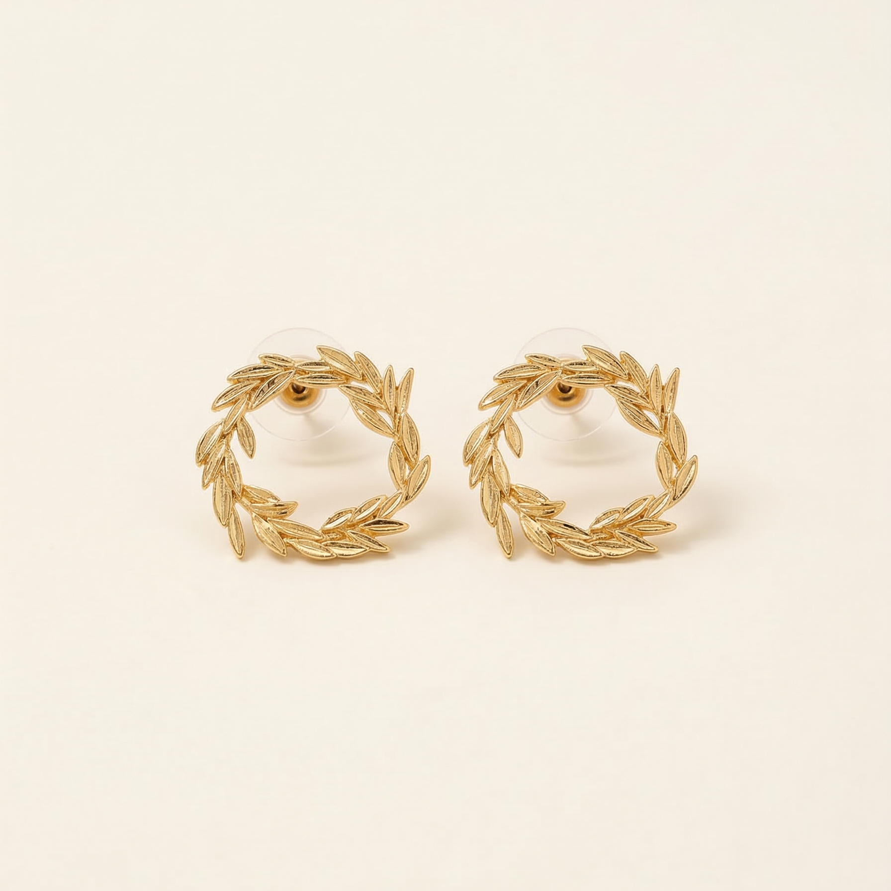 Pair of gold wreath earrings on a beige background