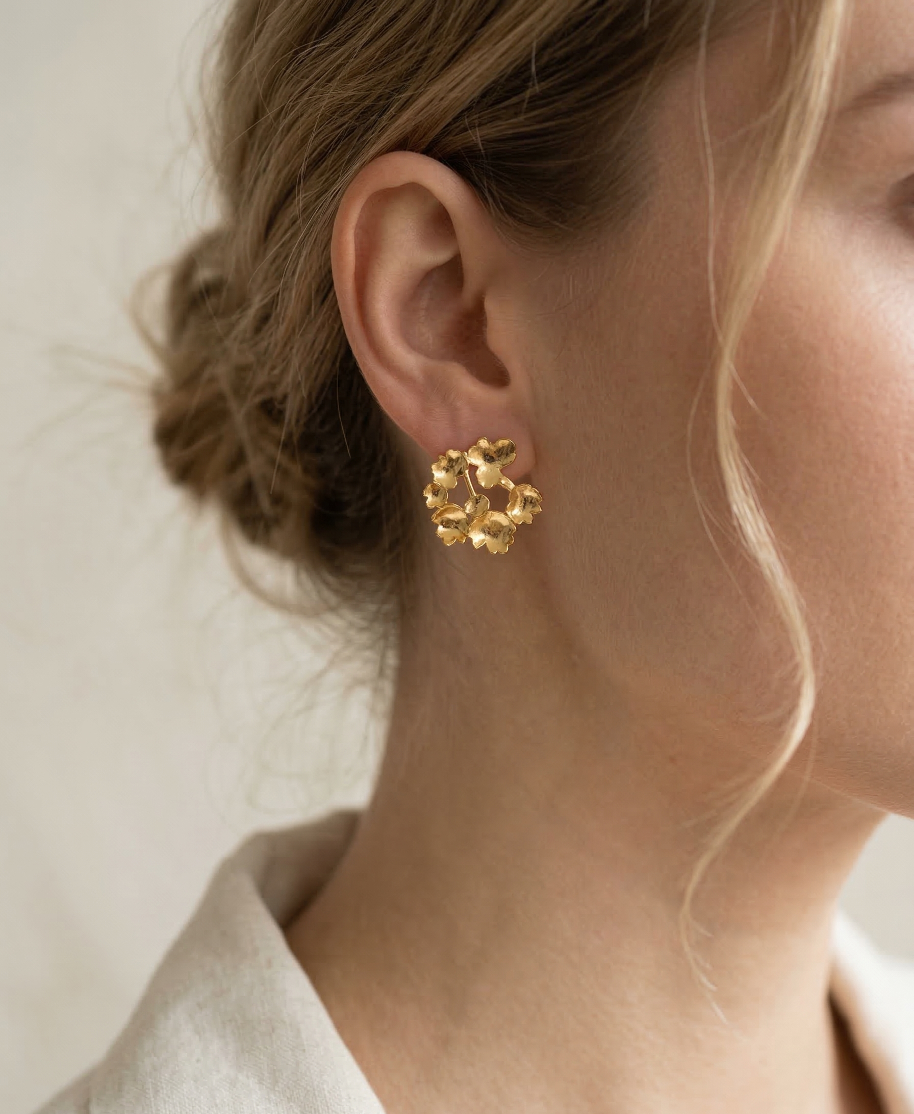 Close-up of a person wearing gold floral earrings with a neutral background