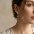 Close-up of a woman wearing gold and silver earrings against a neutral background