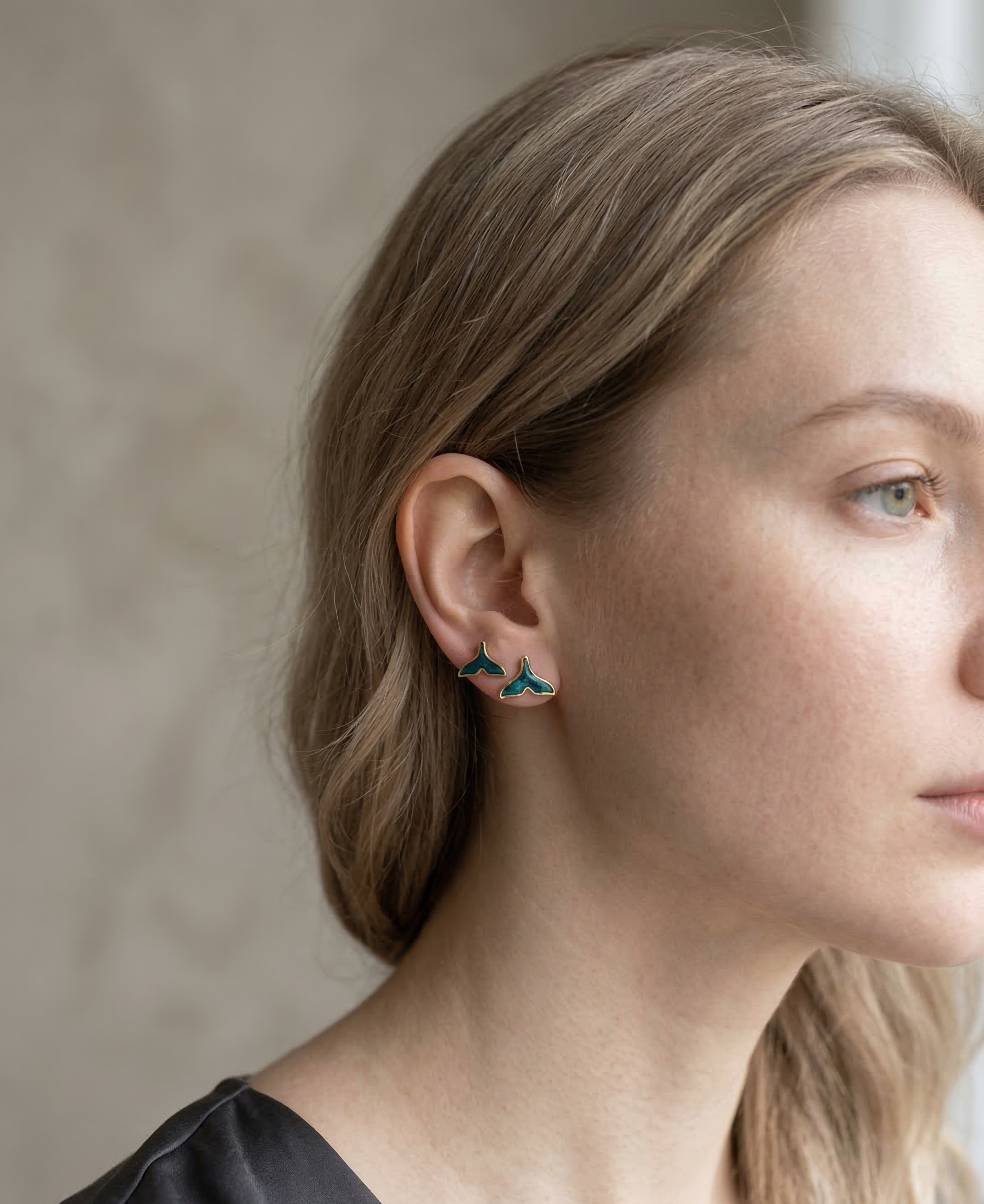 Close-up of a person wearing teal butterfly earrings with a neutral background