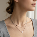 Close-up of a woman wearing a delicate necklace with a heart pendant, set against a neutral background.
