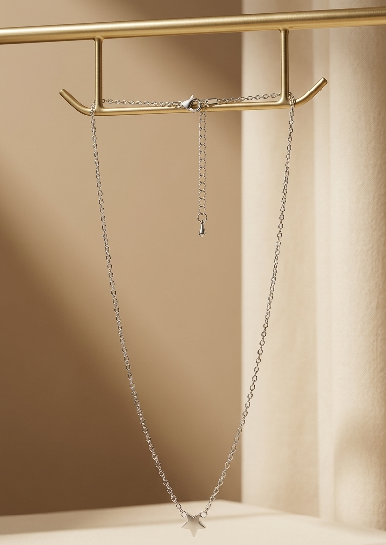 Silver necklace with a star pendant on a gold stand against a beige background
