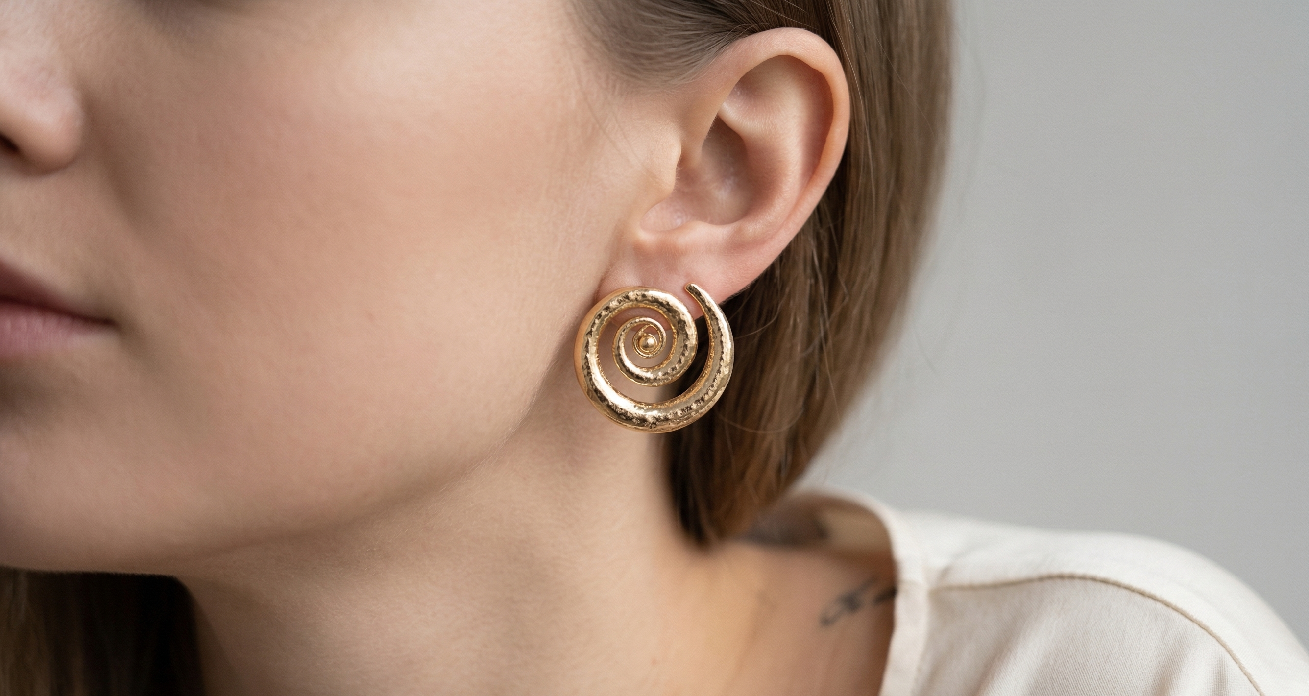 Close-up of a woman wearing gold earrings with a neutral background