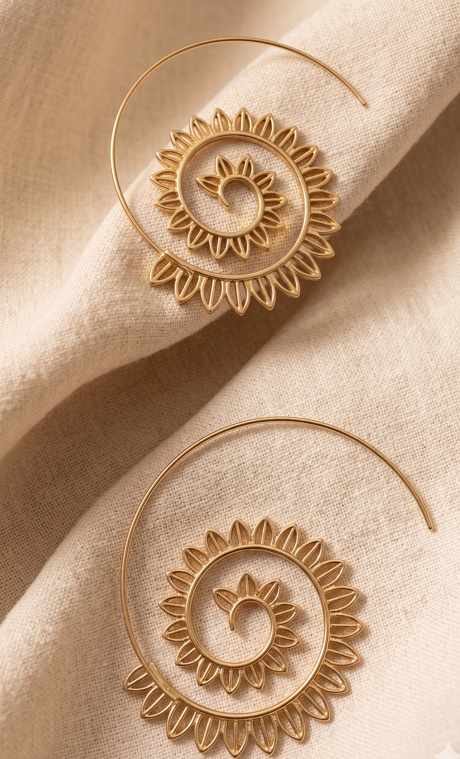 Gold hoop earrings with intricate designs on a beige fabric background