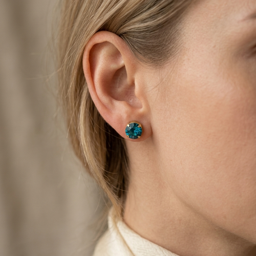 Close-up of a person wearing a blue gemstone earring with a neutral background
