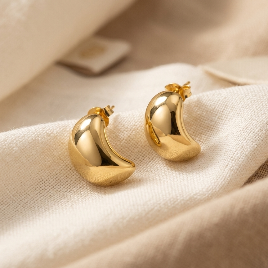 Gold earrings on a beige fabric background