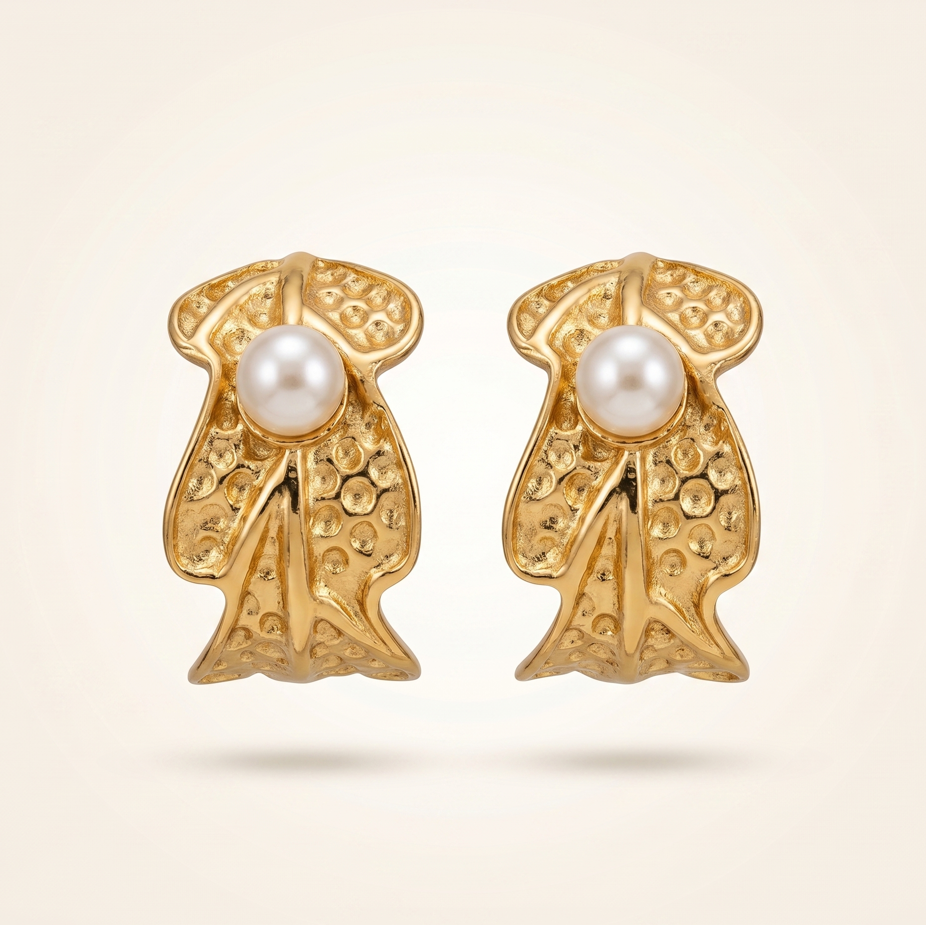 Gold earrings with pearl centers on a beige background