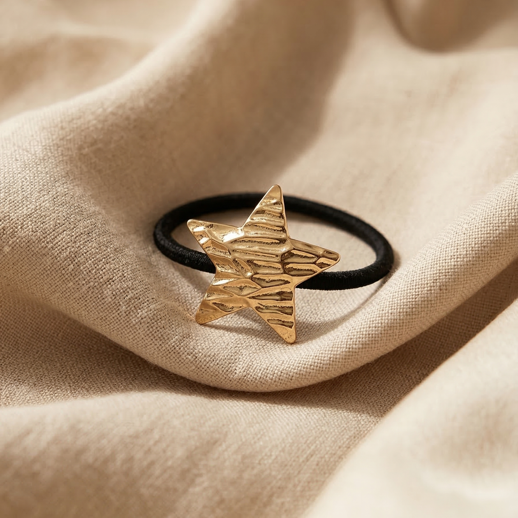 Gold star-shaped hair tie on a beige fabric background