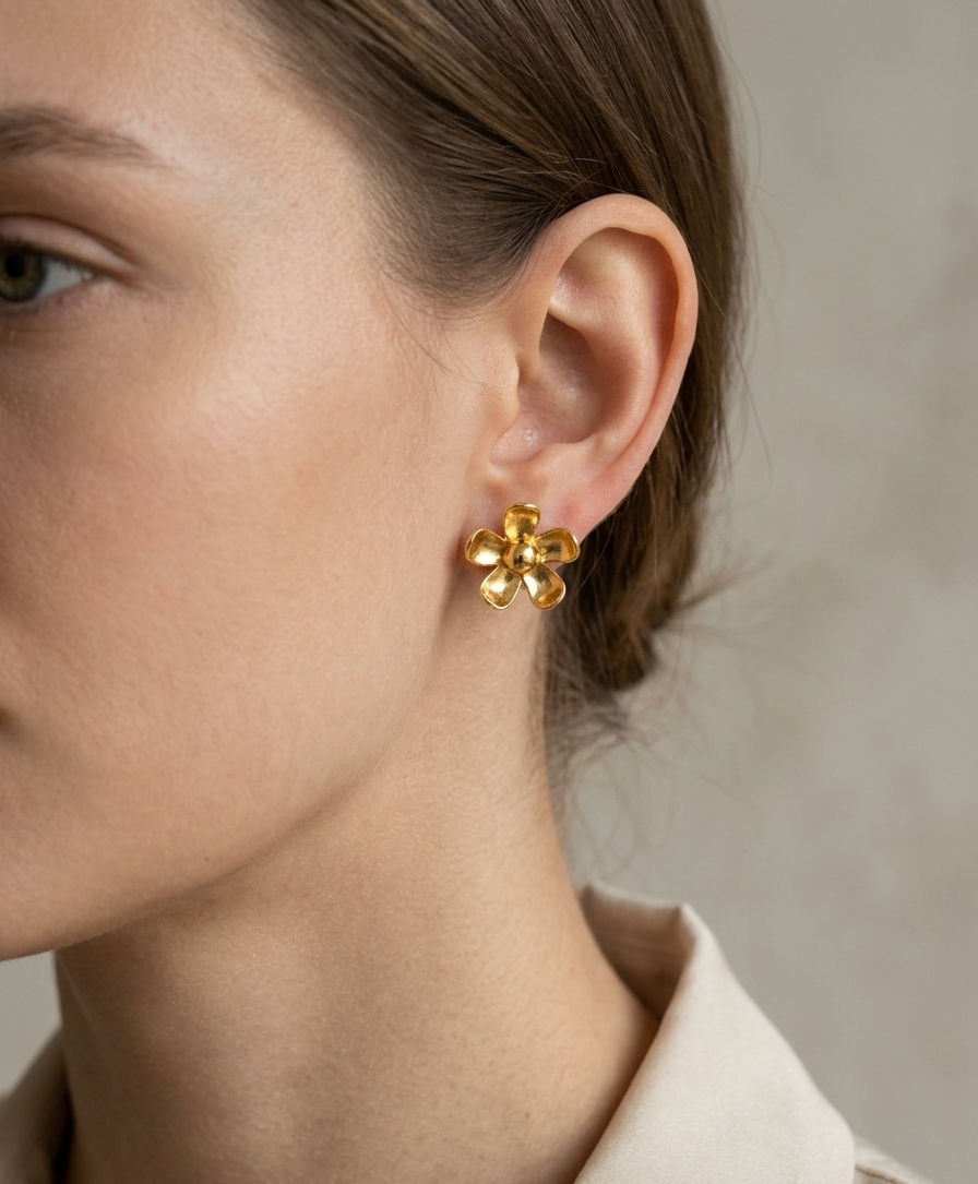 Gold flower-shaped earring worn by a person with a neutral background